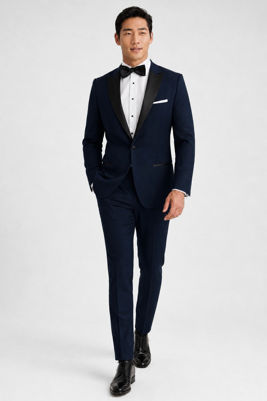Man wearing a navy tuxedo with a white shirt and black bow tie on a white background
