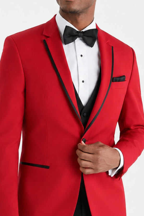 A man wearing a bright red tuxedo jacket with black satin lapels, a black vest, a white dress shirt, and a black bow tie, photographed against a light gray studio background.